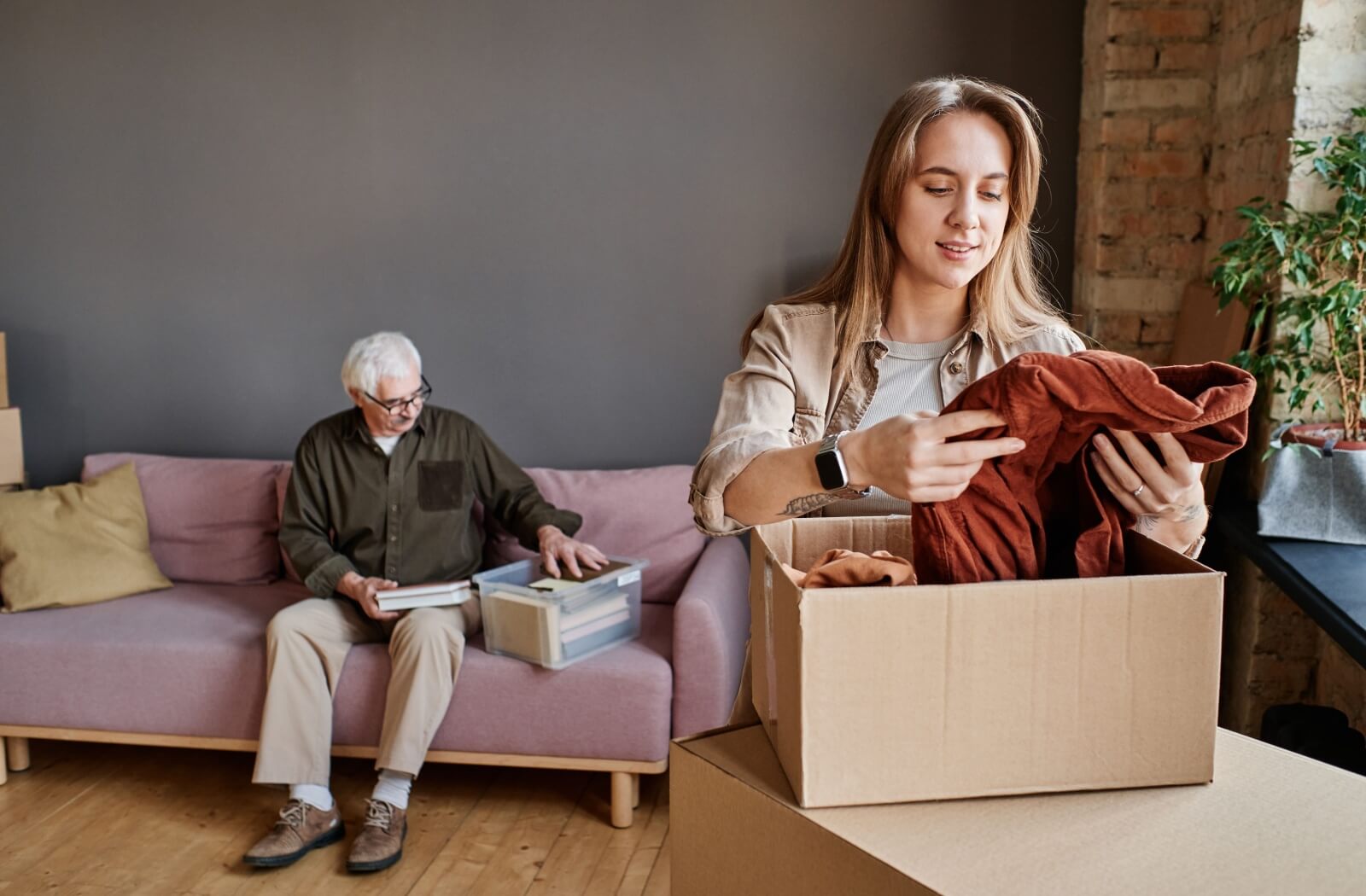 A young woman helping her older adult father downsize by sorting through boxes of clothing.