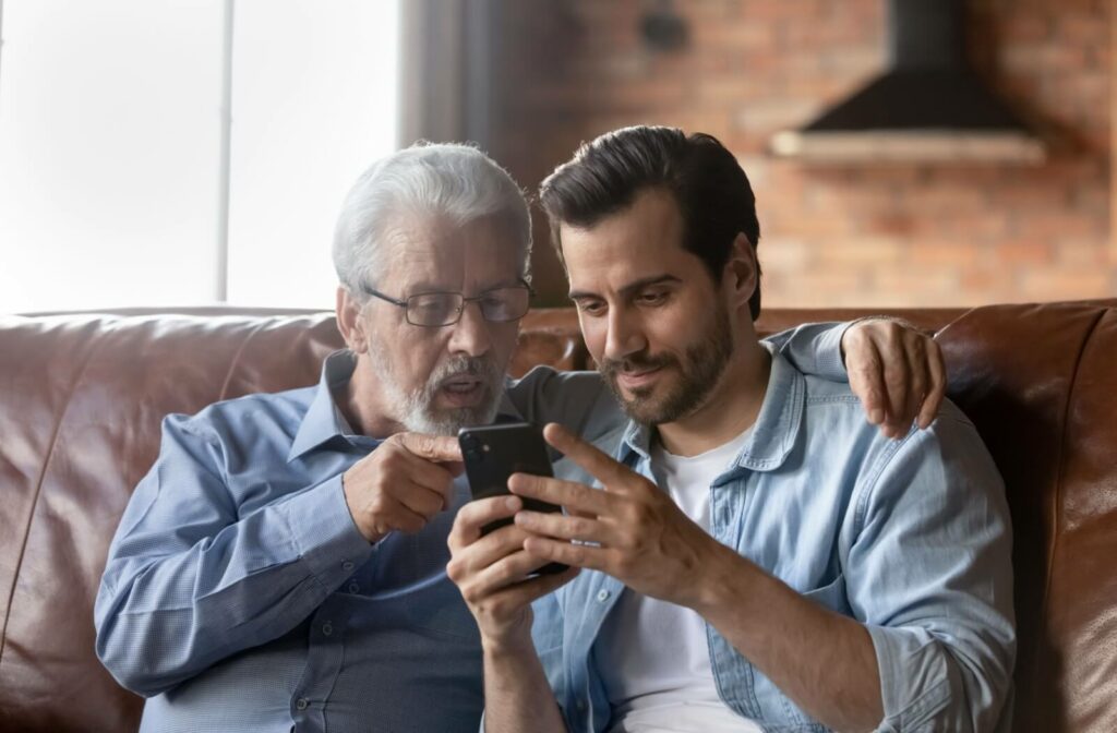 An adult son shows his father something on the screen of his smartphone in a memory care community.