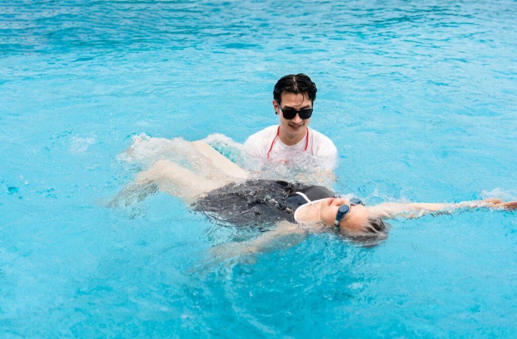 A swim instructor helps an older adult with their water aerobics.