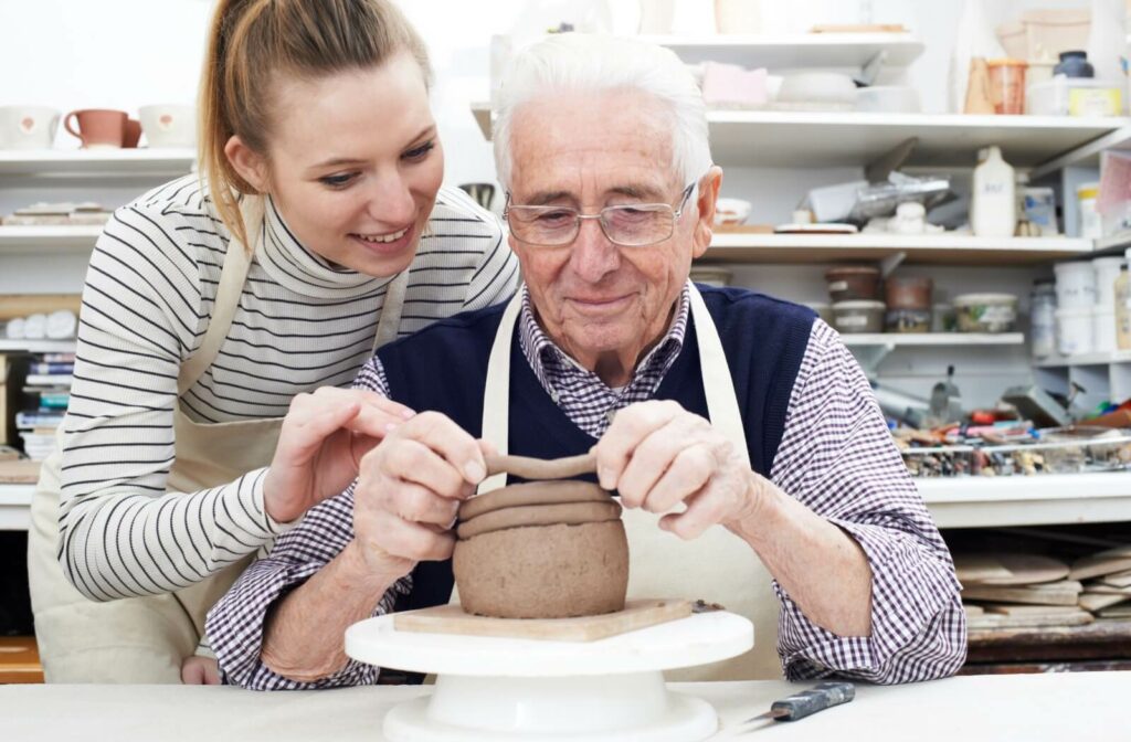 An older adult and their grandchild joyfully crafting pottery together in a community space.