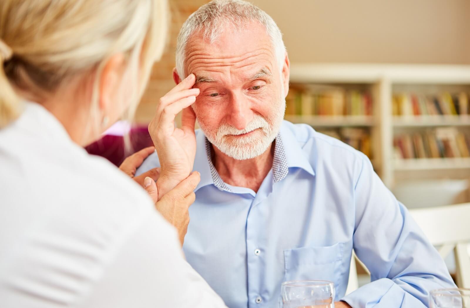 An older adult rubs their forehead in confusion during an appointment with a healthcare professional