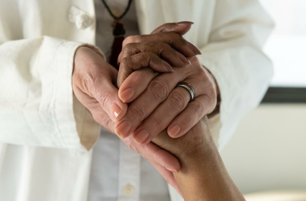 A caregiver clasps the hand of an older adult during a healthcare checkup in memory care