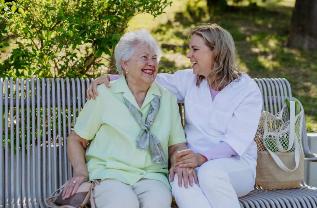 A caregiver and their parent with dementia sitting on a park bench and holding each other lovingly.