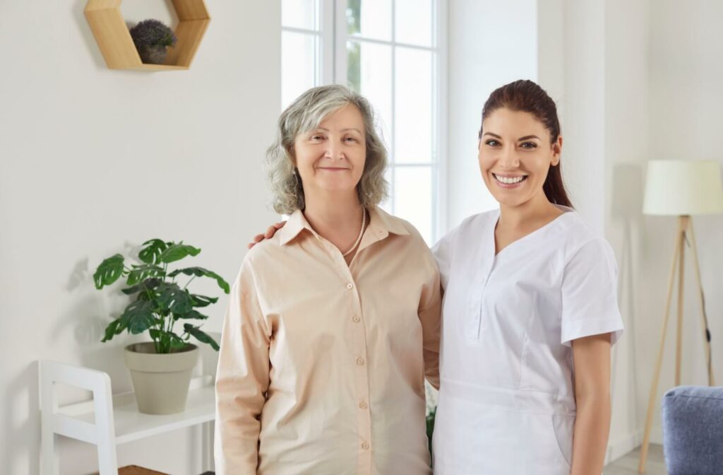 Smiling older adult standing beside supportive caregiver in bright room with plants and natural light
