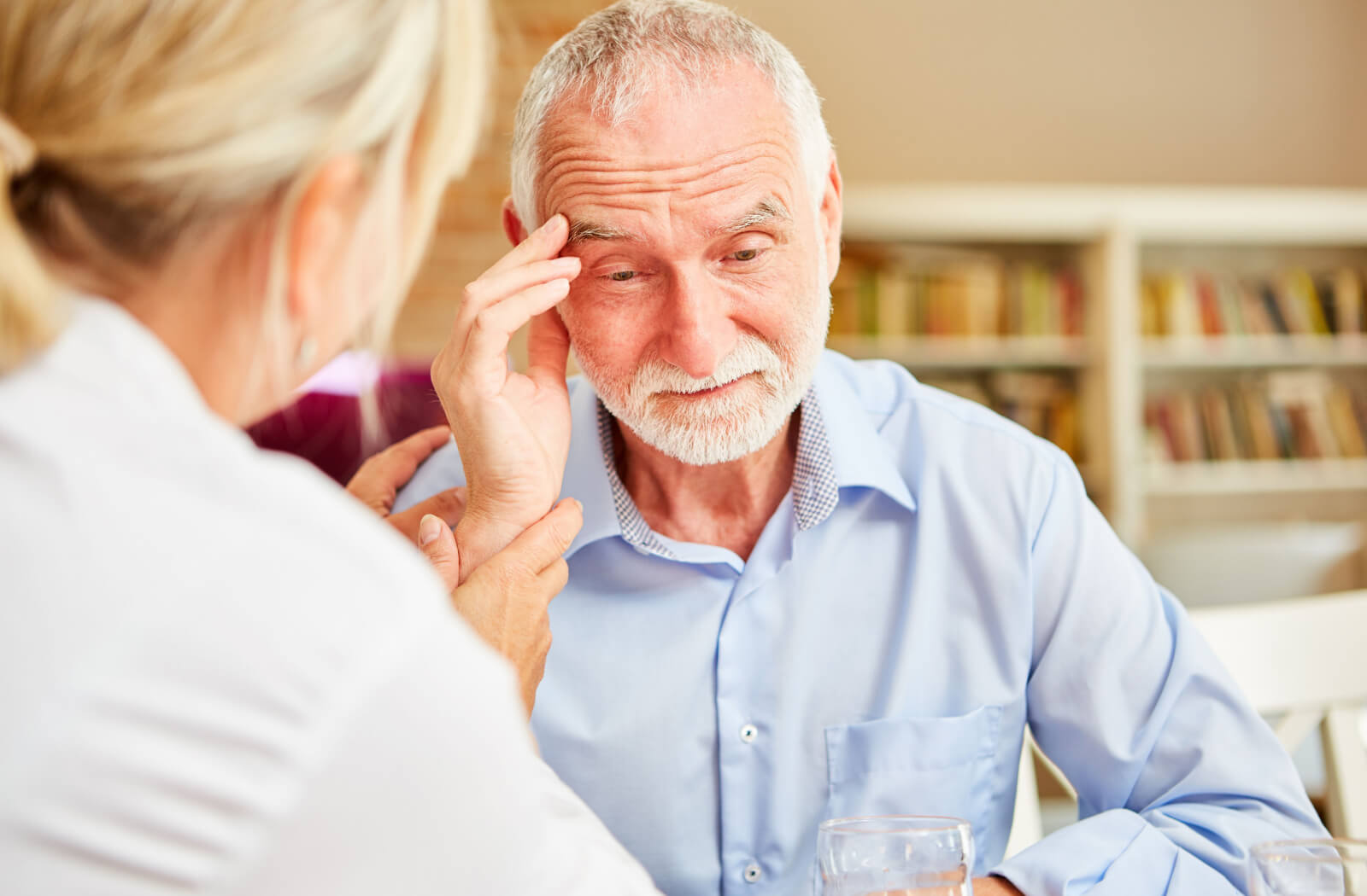 An older adult rubs their forehead in confusion during an appointment with a healthcare professional