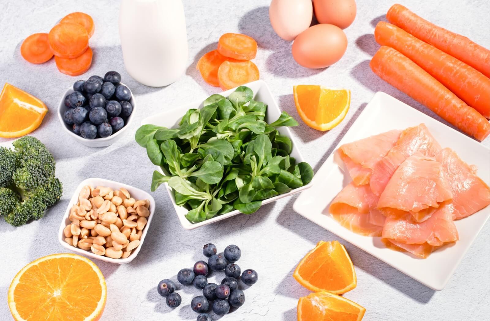 A table full of healthy food for brain health, including spinach, blueberries, oranges, peanuts, and carrots.